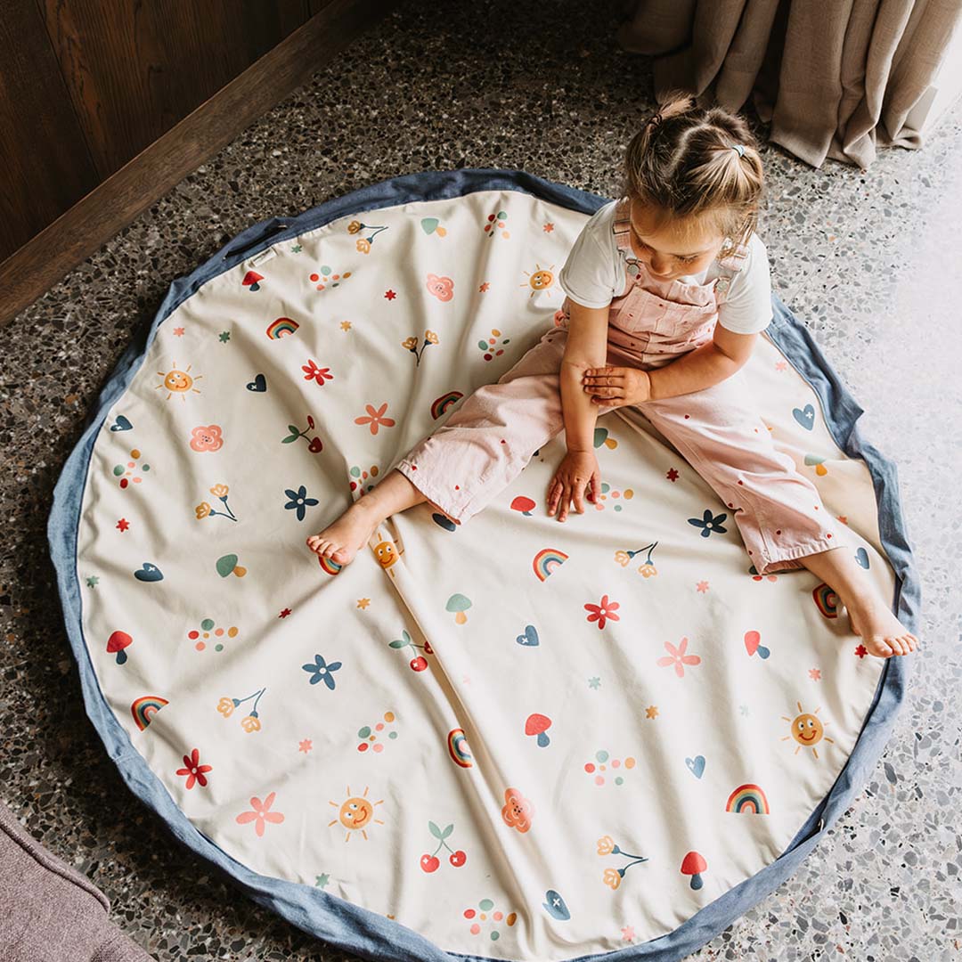 Een kind zit op het uitgespreide play&go speelkleed met bloemen, harten en regenbogen.