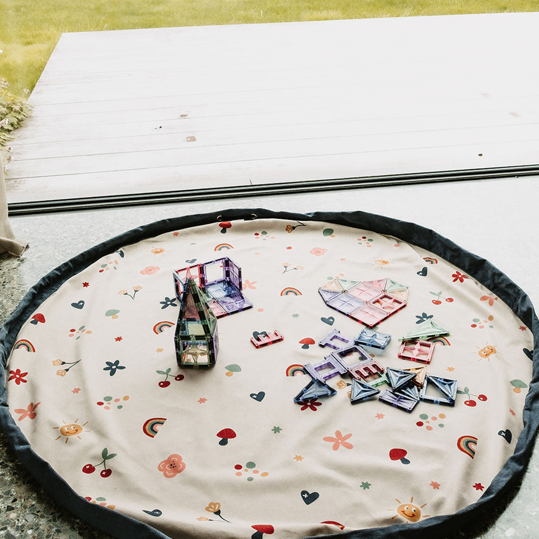 Het play&go speelkleed met bloemen, harten en regenbogen ligt uitgespreid met magnetische bouwtegels erop.