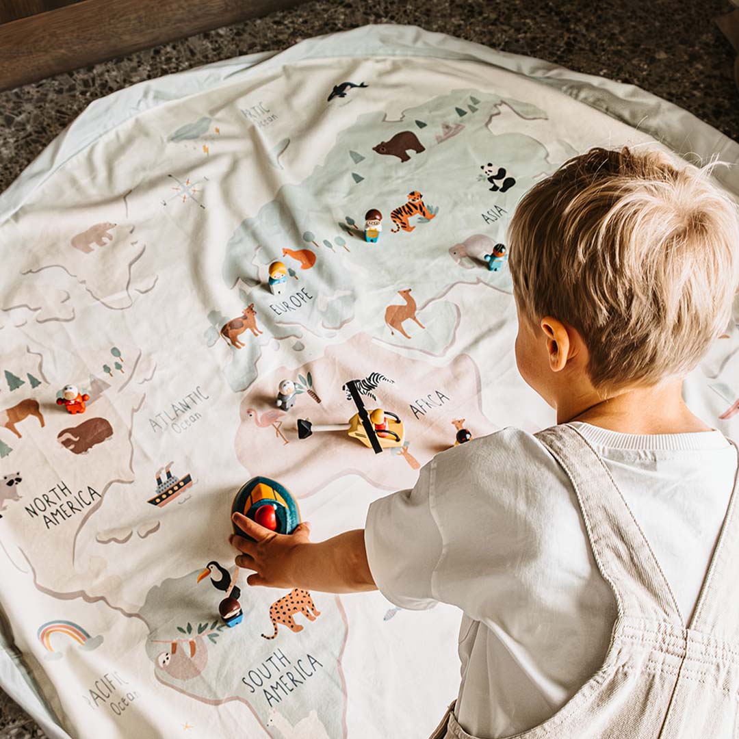 Een kind speelt op het Play&Go speelkleed met wereldkaartpatroon en kleine dierenfiguren.