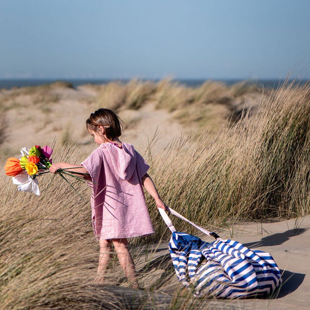 Een kind trekt de play&go gestreepte opbergzak met speelgoed door de duinen.