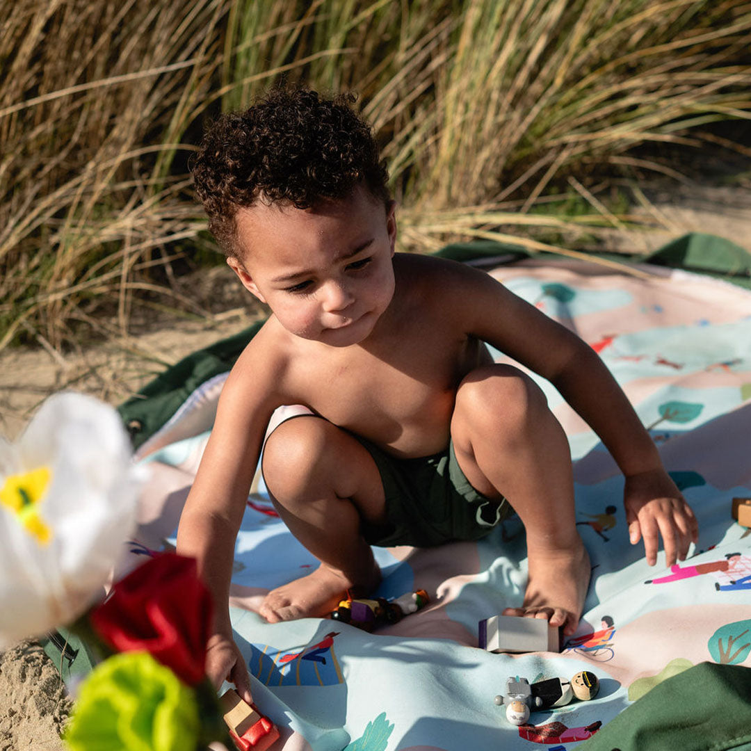 Een jong kind speelt met houten speelgoed op het play&go speelkleed met parkthema op het strand.