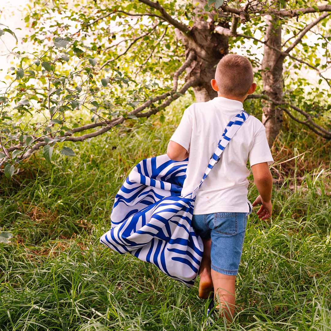 Een kind draagt de play&go opbergzak met golfpatroon als schoudertas door het gras.