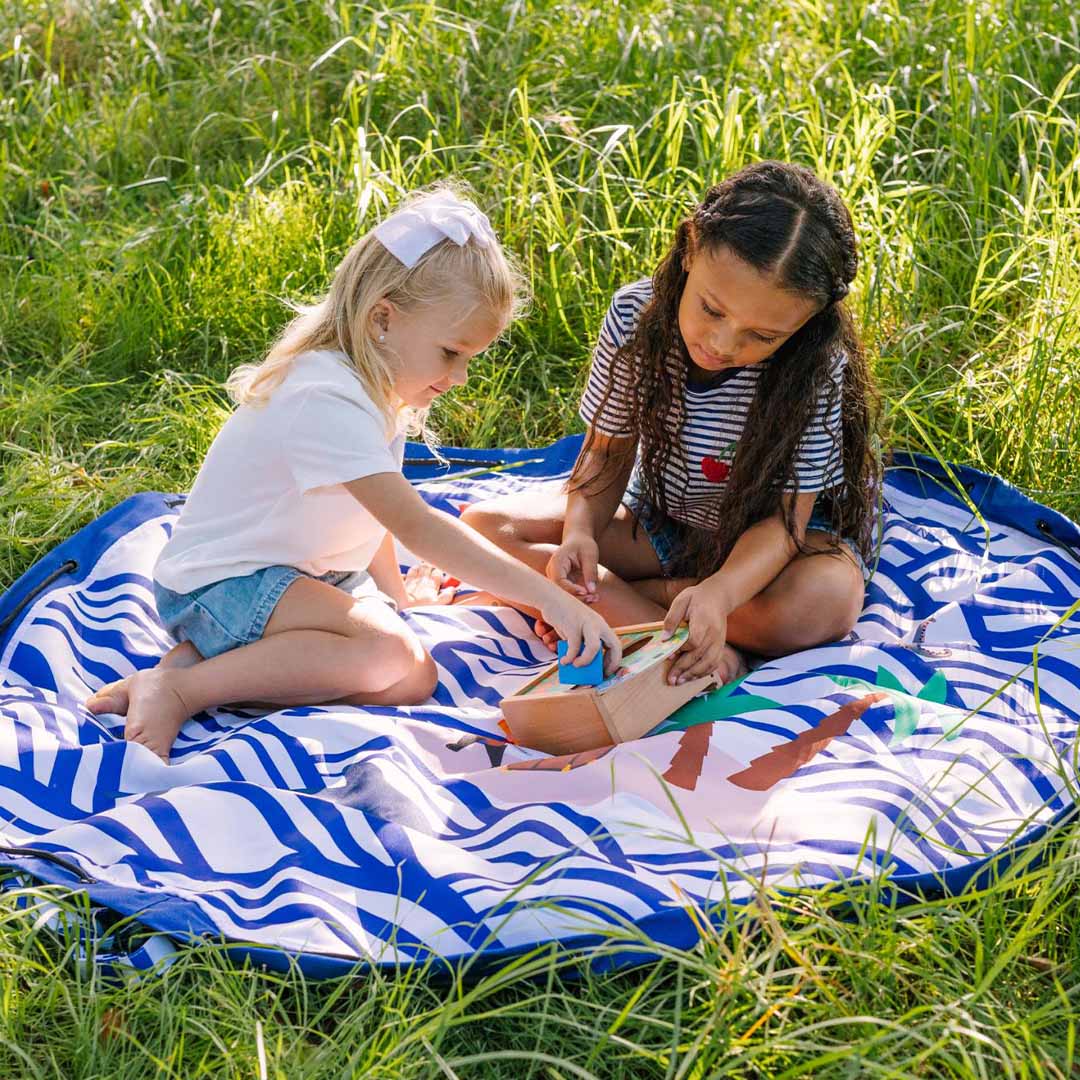 Twee kinderen spelen op het uitgespreide speelkleed met golfpatroon in het gras.
