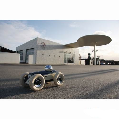 De Playforever raceauto Clyde staat op asfalt voor een modern tankstation.