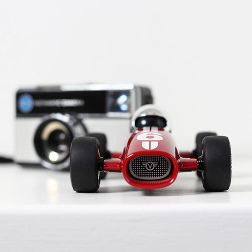 Playforever rode raceauto met nummer 6 staat voor een vintage camera op een witte ondergrond.