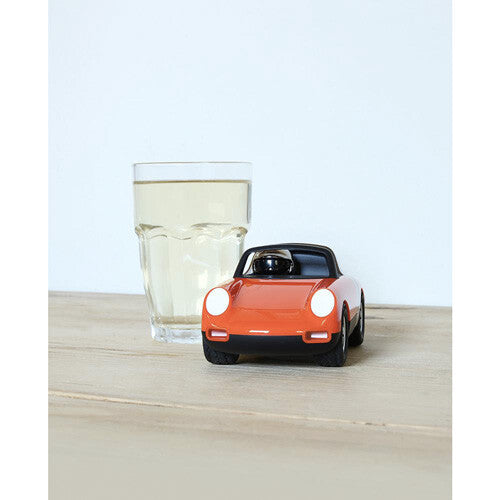 Playforever speelgoedauto Luft Biba in oranje en zwart, naast een glas water op een houten tafel.