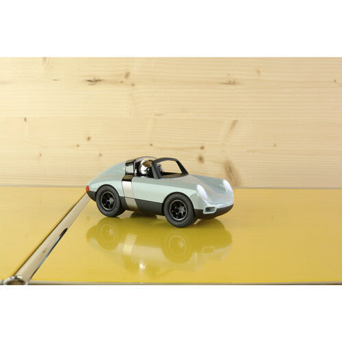 Playforever speelgoedauto op een glanzende gele ondergrond voor een houten wand.
