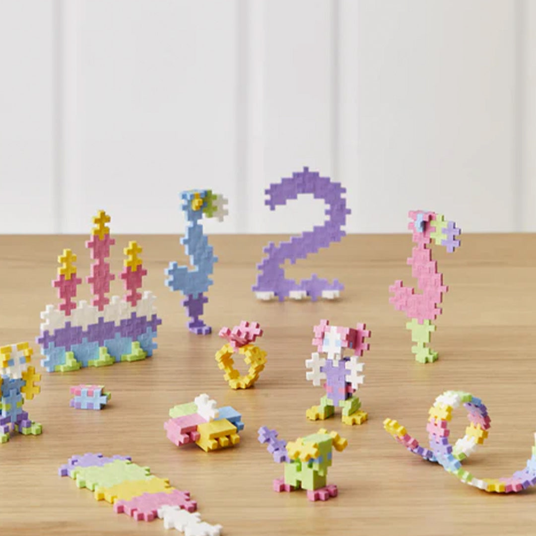 Diverse kleine creaties van pastelkleurige Plus-Plus bouwblokken, waaronder een taart en cijfers.