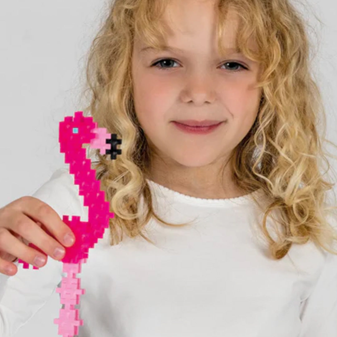 Een lachend meisje houdt een roze flamingo vast, gemaakt van Plus-Plus bouwstenen.