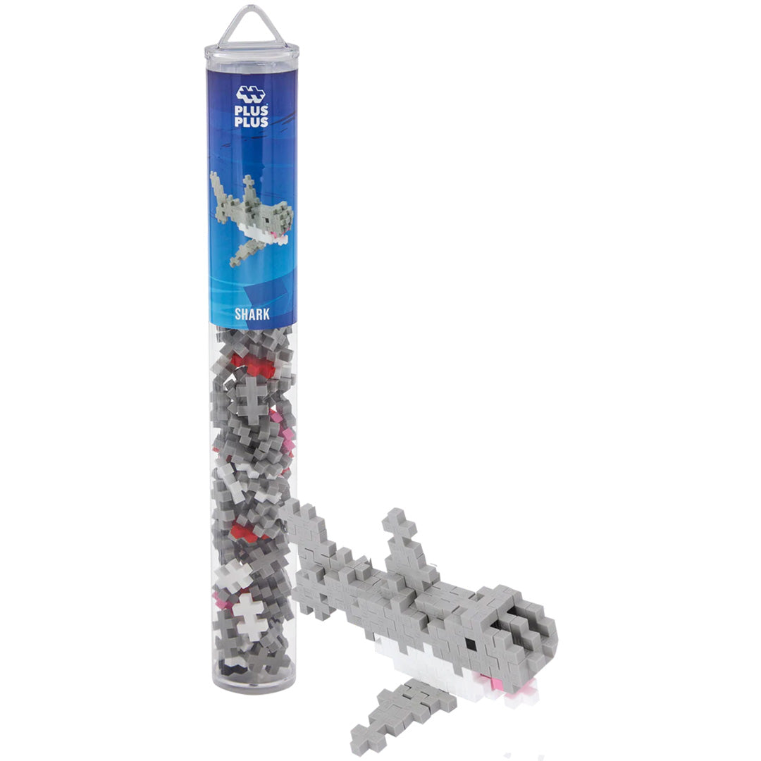 Plus-Plus bouwstenen set met een transparante koker vol grijze, witte en roze bouwblokken en een gebouwde haai ernaast.