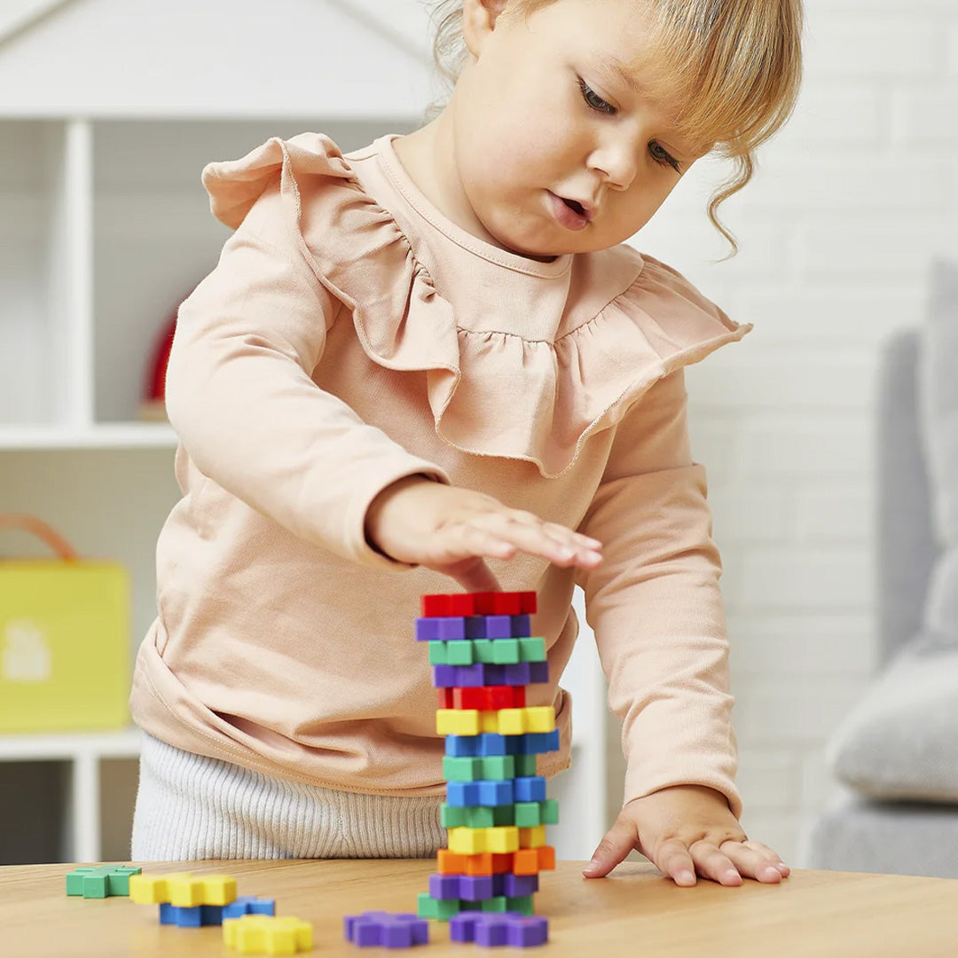 Een peuter stapelt kleurrijke Plus-Plus BIG bouwstenen tot een toren op een houten tafel.