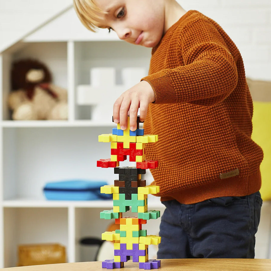 Een jongen bouwt een toren met kleurrijke Plus-Plus BIG bouwstenen op een houten tafel.