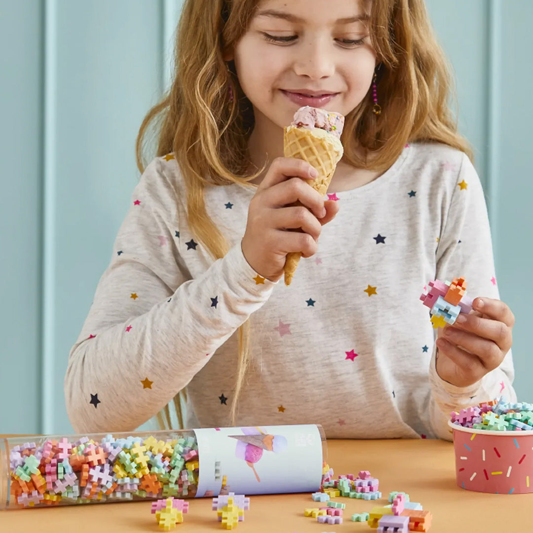 Een meisje eet een ijshoorntje en speelt met Plus-Plus bouwblokken in gelato kleuren.