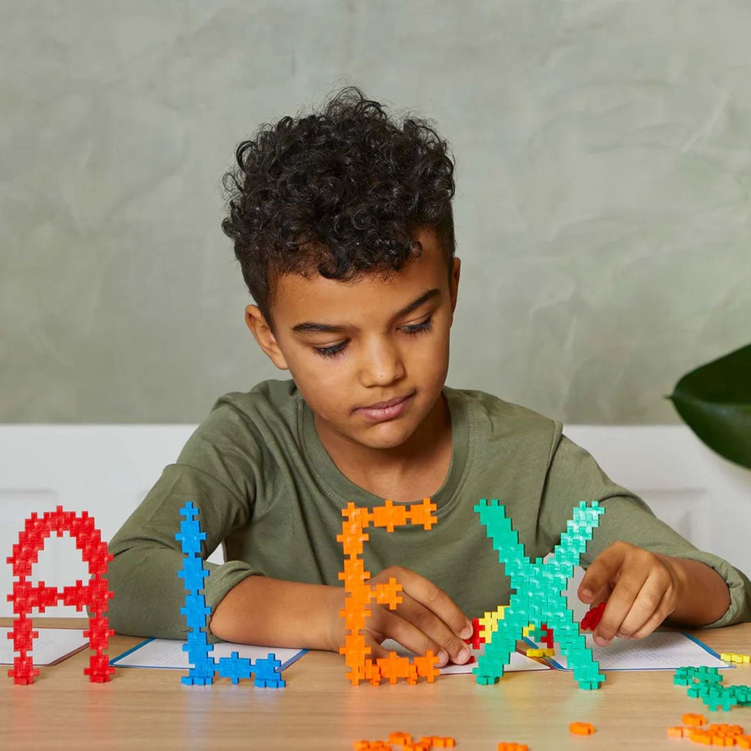 Jongen bouwt de letters A, L, E en X met Plus-Plus bouwblokken.