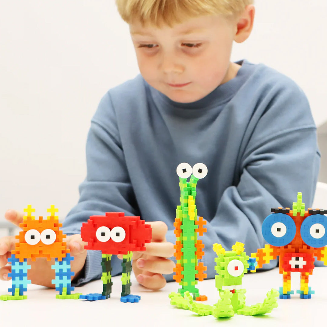 Een jongen speelt met vier kleurrijke Plus-Plus monsterfiguren op een witte tafel.