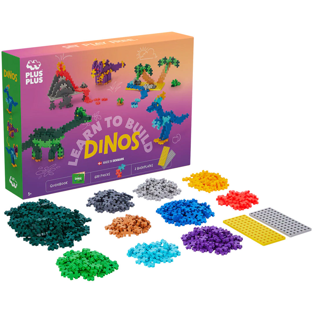 De verpakking van de Plus-Plus bouwstenen 'Learn to Build Dinos' set met daarnaast losse Plus-Plus bouwblokken in verschillende kleuren en twee bouwplaten.