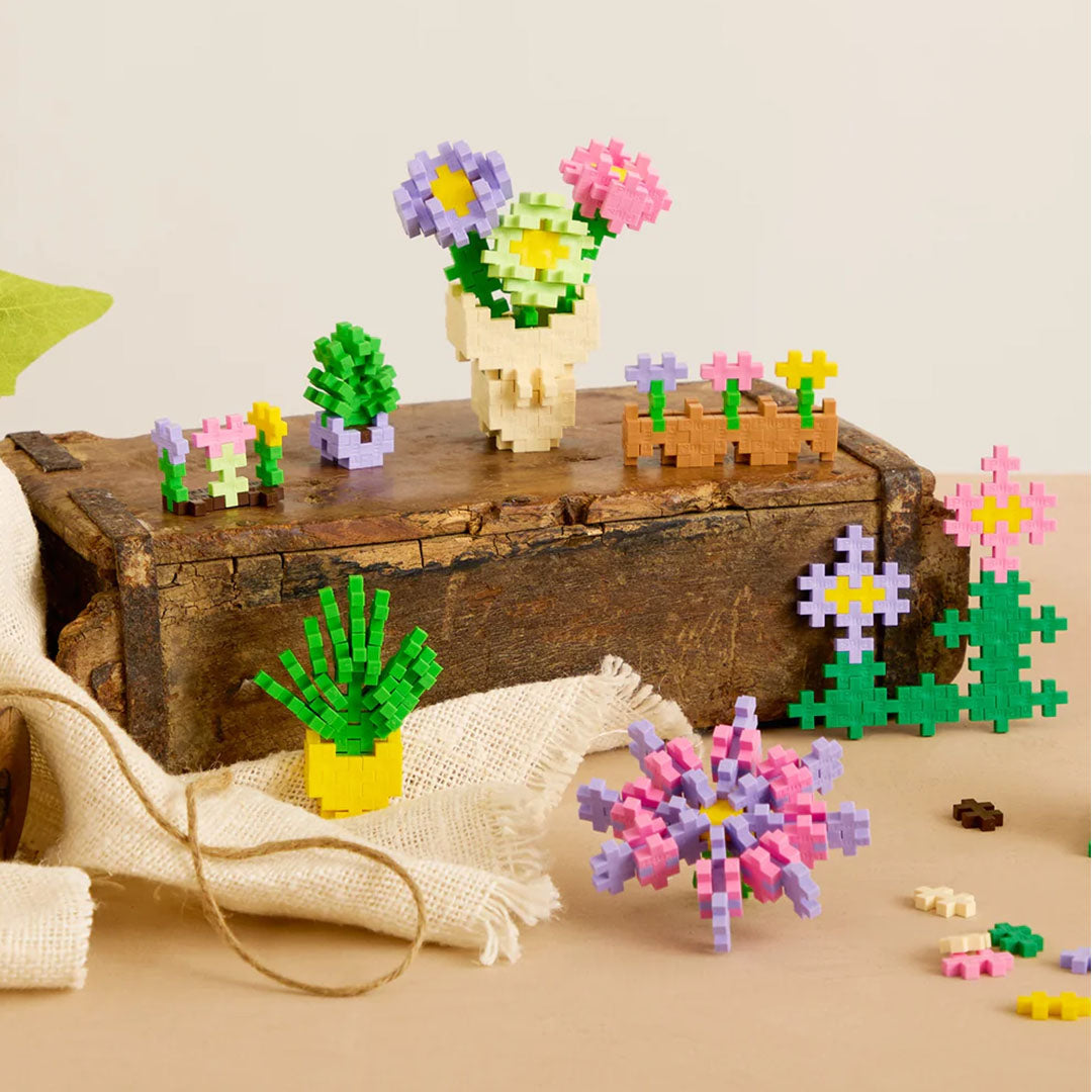 Een collectie van Plus-Plus bouwspeelgoed bloemen en planten creaties op een houten kist.