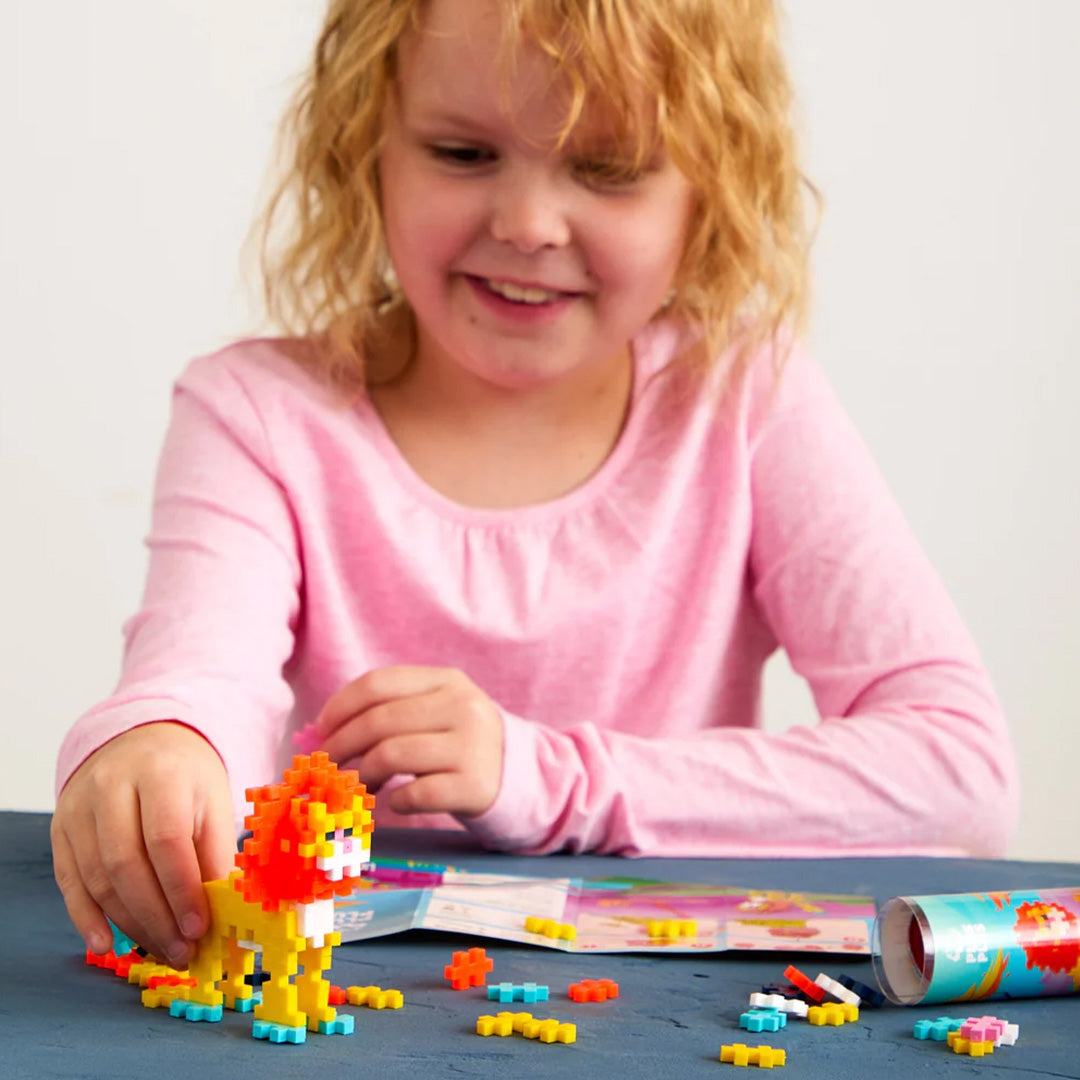 Een kind bouwt een leeuwfiguur met Plus-Plus bouwstenen aan tafel.