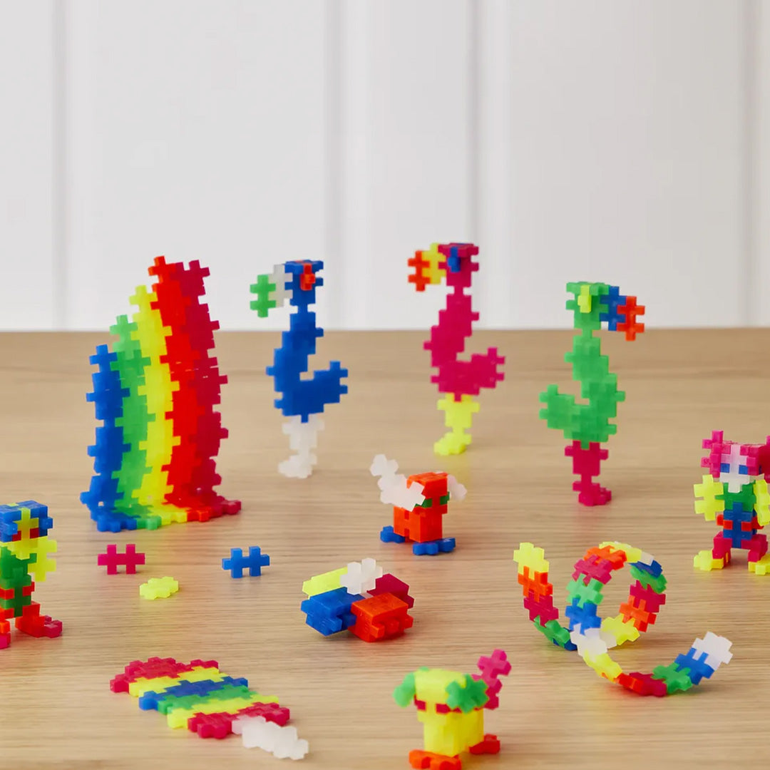Diverse figuren en vormen gemaakt van Plus-Plus neon bouwblokken op een houten tafel.