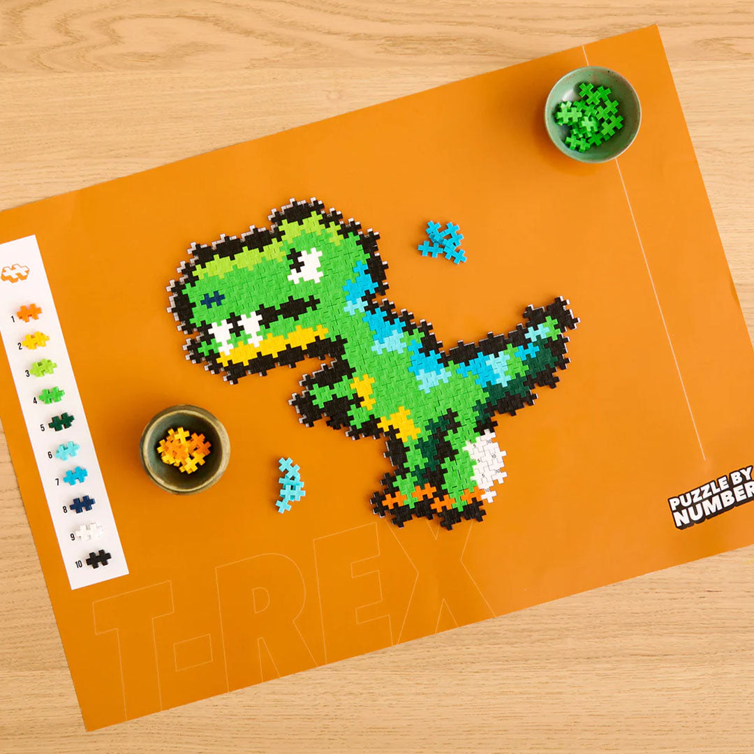Een Plus-Plus T-Rex figuur in aanbouw op een oranje puzzelmat, met losse bouwstenen in schaaltjes.