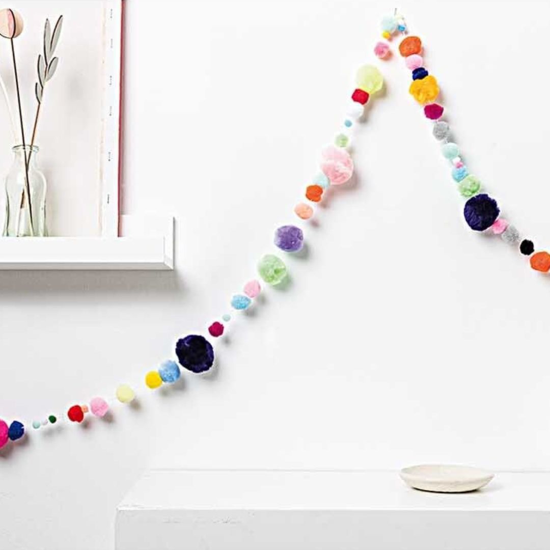 Een kleurrijke slinger van pompons hangt tegen een witte muur als decoratie.
