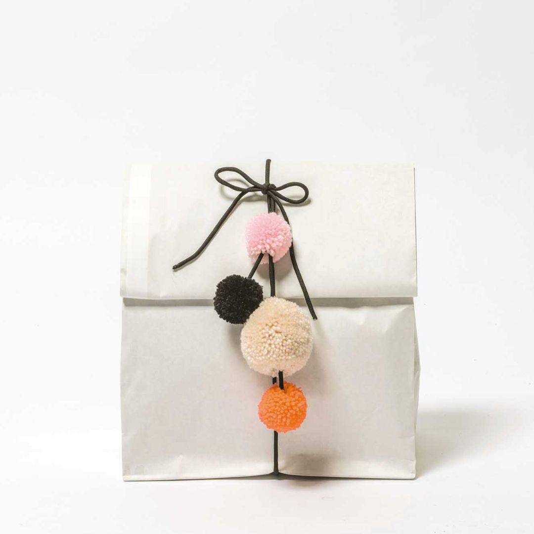 Een wit papieren cadeauzakje versierd met een slinger van vier gekleurde pompons.