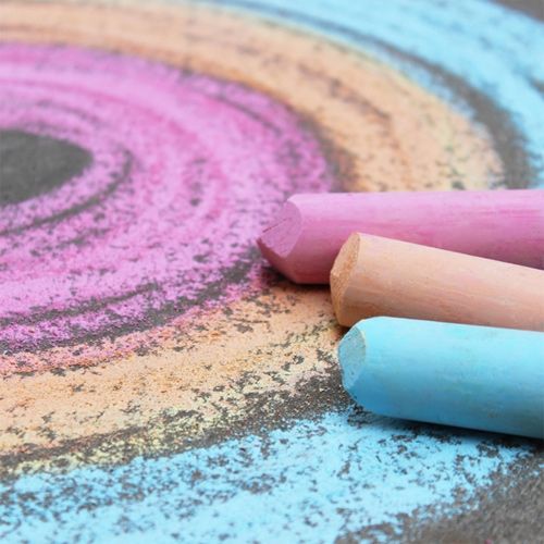Drie gekleurde stoepkrijtjes liggen naast een kleurrijke krijttekening op de grond.