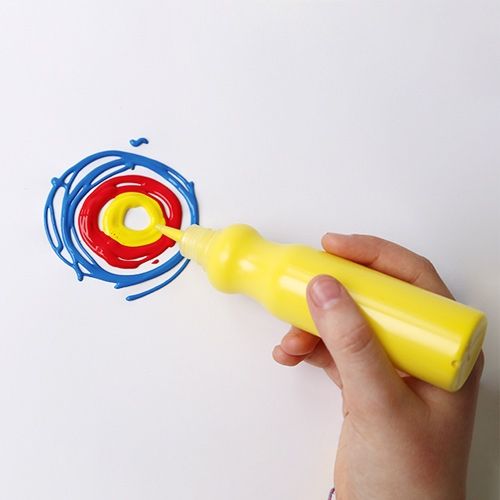 Een hand knijpt gele Primo plakkaatverf uit een fles op een wit oppervlak, met rode en blauwe verf eromheen.