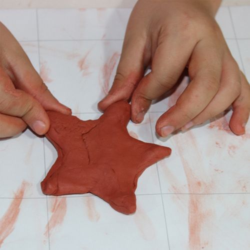 Twee handen vormen een ster van terracotta modelleerklei.