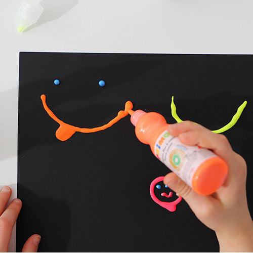 Een hand tekent een lachend gezichtje met oranje Primo plakkaatverf op een zwarte ondergrond.