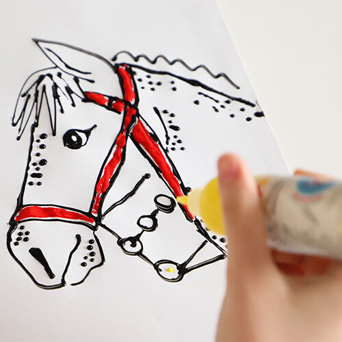 Een hand kleurt een paardenhoofd met rode teugels in met gele verf uit een knijpflesje.
