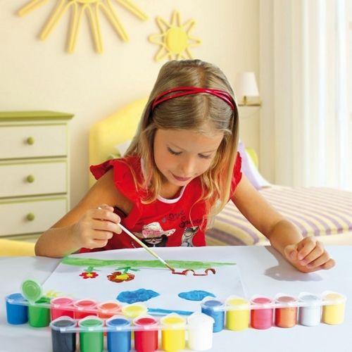 Een meisje schildert met een kwast op papier, met een rij kleurrijke potjes plakkaatverf voor haar op tafel.