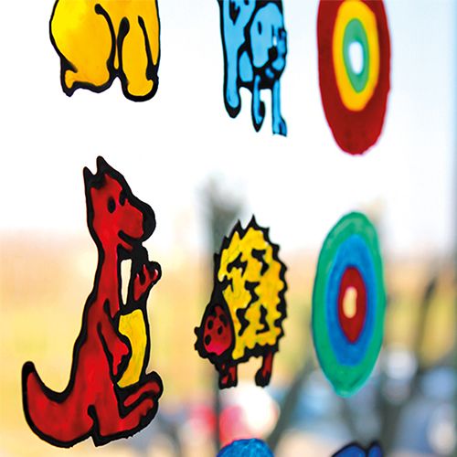 Kleurrijke raamverf creaties van dieren en cirkels geplakt op een raam.