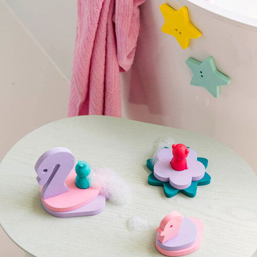 De quut badpuzzel met schuimfiguren van een zwaan, bloem en eend op een tafeltje, en sterren op de badrand.