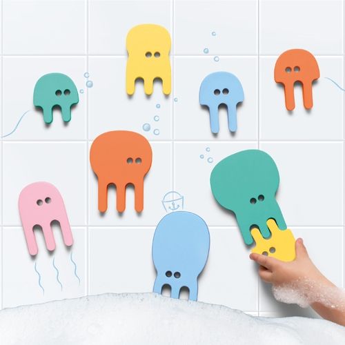 Een kind speelt met Quut badpuzzel kwallen in een bad met schuim, waarbij de kleurrijke kwallen aan de tegelwand plakken.