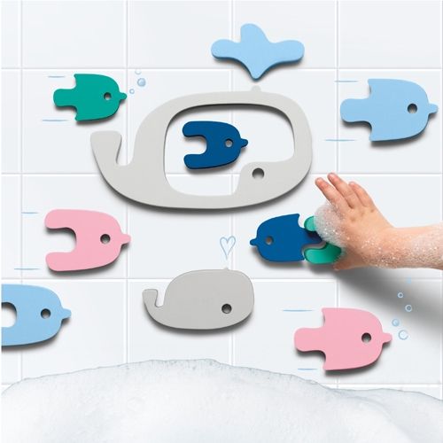 Quut badpuzzel met walvissen en vissen van schuim op witte tegels, met een kinderhand die speelt.