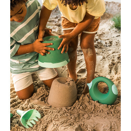 Twee kinderen maken zandkastelen met groene zandbakspeeltjes in het zand.