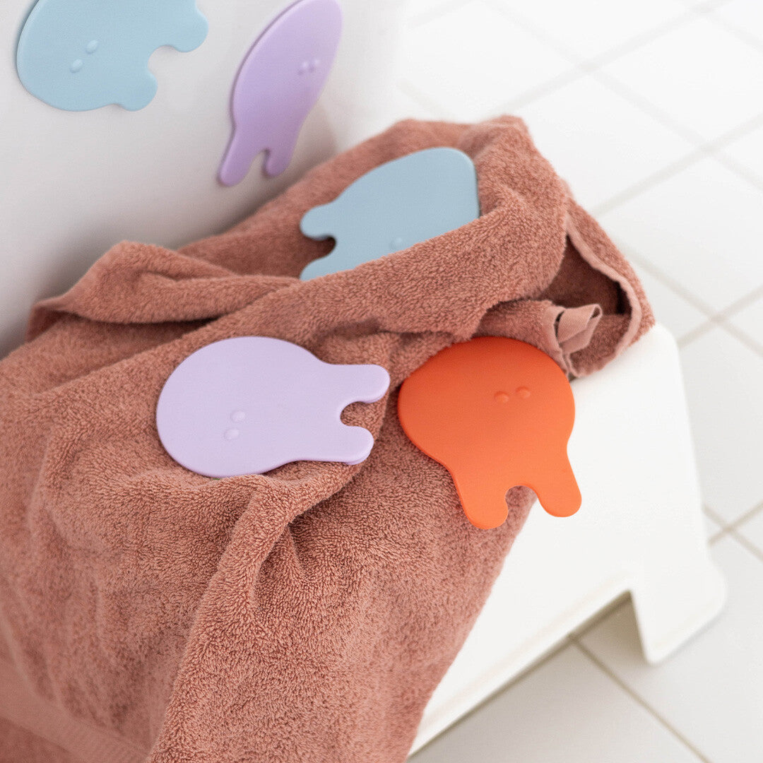 Drie Quut Grippi antislip badmatjes in de vorm van kwallen liggen op een bruine handdoek.