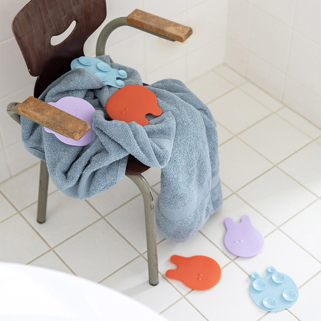 Meerdere Quut Grippi antislip badmatjes in de vorm van kwallen liggen op een handdoek en op de badkamervloer.
