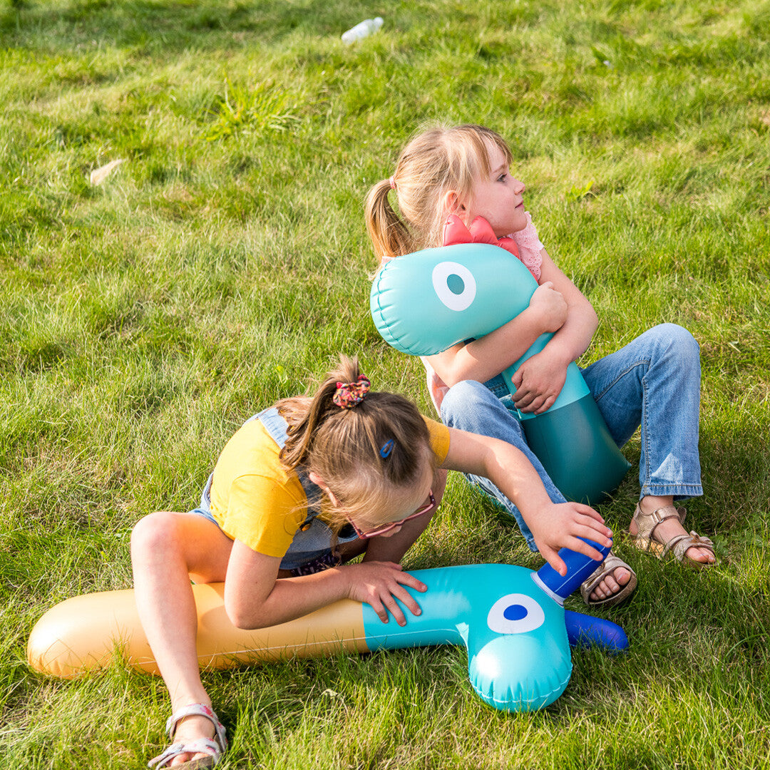 Twee meisjes spelen op het gras met twee quut opblaasbare giraffe speelfiguren.