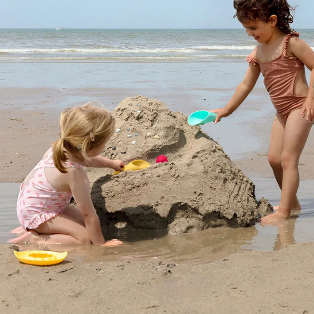 Twee kinderen spelen op het strand met de quut Cuppi schep met zeef en bal.