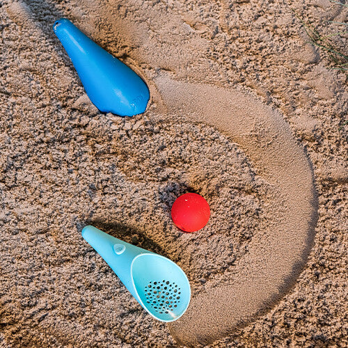 Twee quut scheppen en een rode bal liggen in het zand, met een cirkel eromheen getekend.
