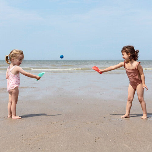 Twee kinderen spelen op het strand met de quut scheppen als rackets en een blauwe bal.