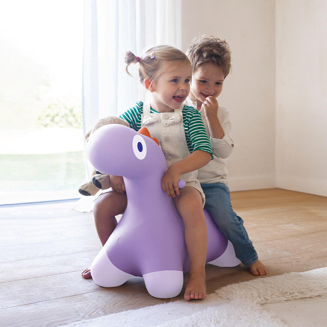 Twee lachende kinderen spelen binnenshuis met het Quut paarse dinosaurusskippydier.