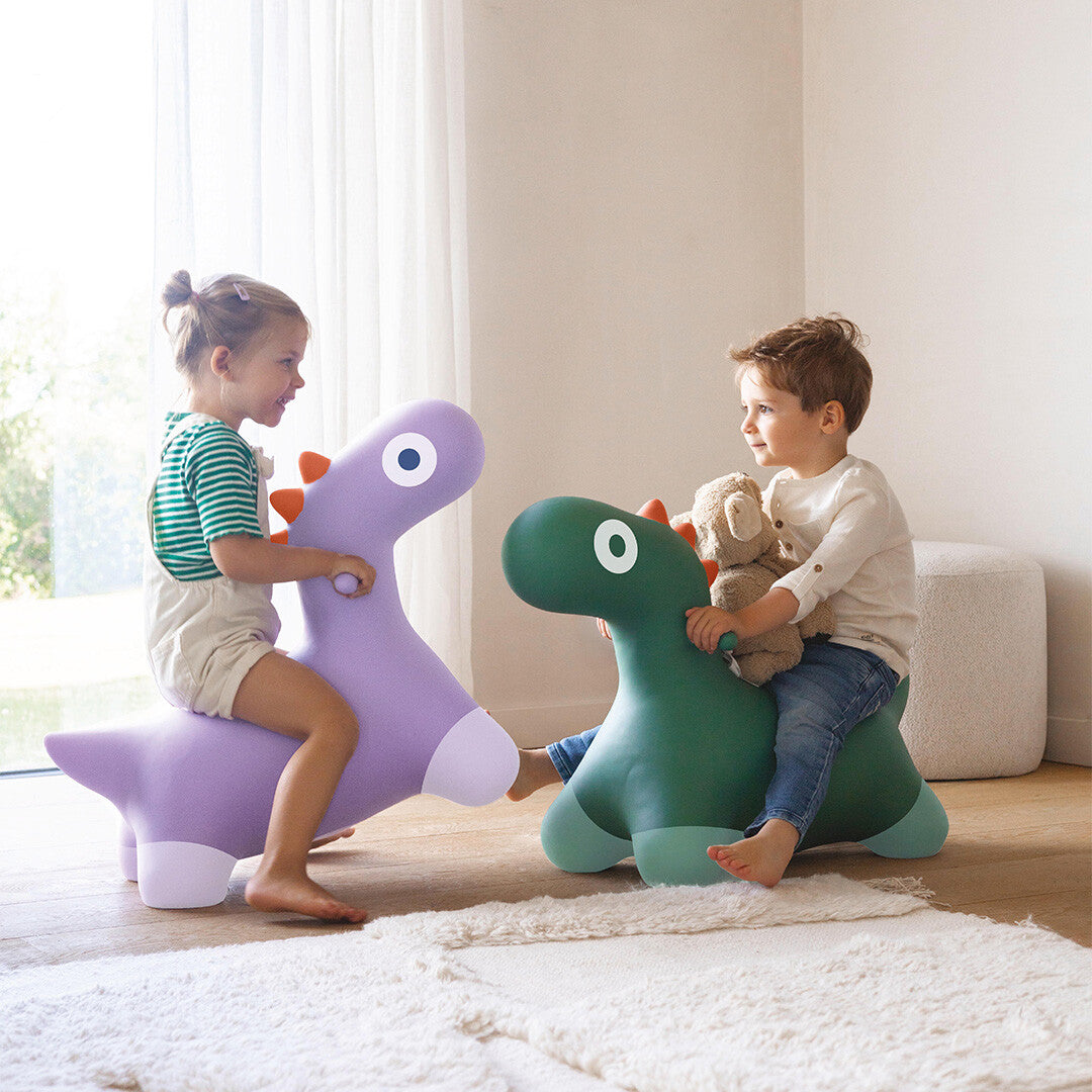 Twee kinderen rijden binnenshuis op een paars en een groen Quut dinosaurusskippydier.