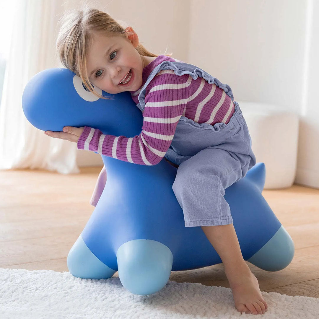 Een lachend meisje zit op het blauwe opblaasbare dino skippydier.