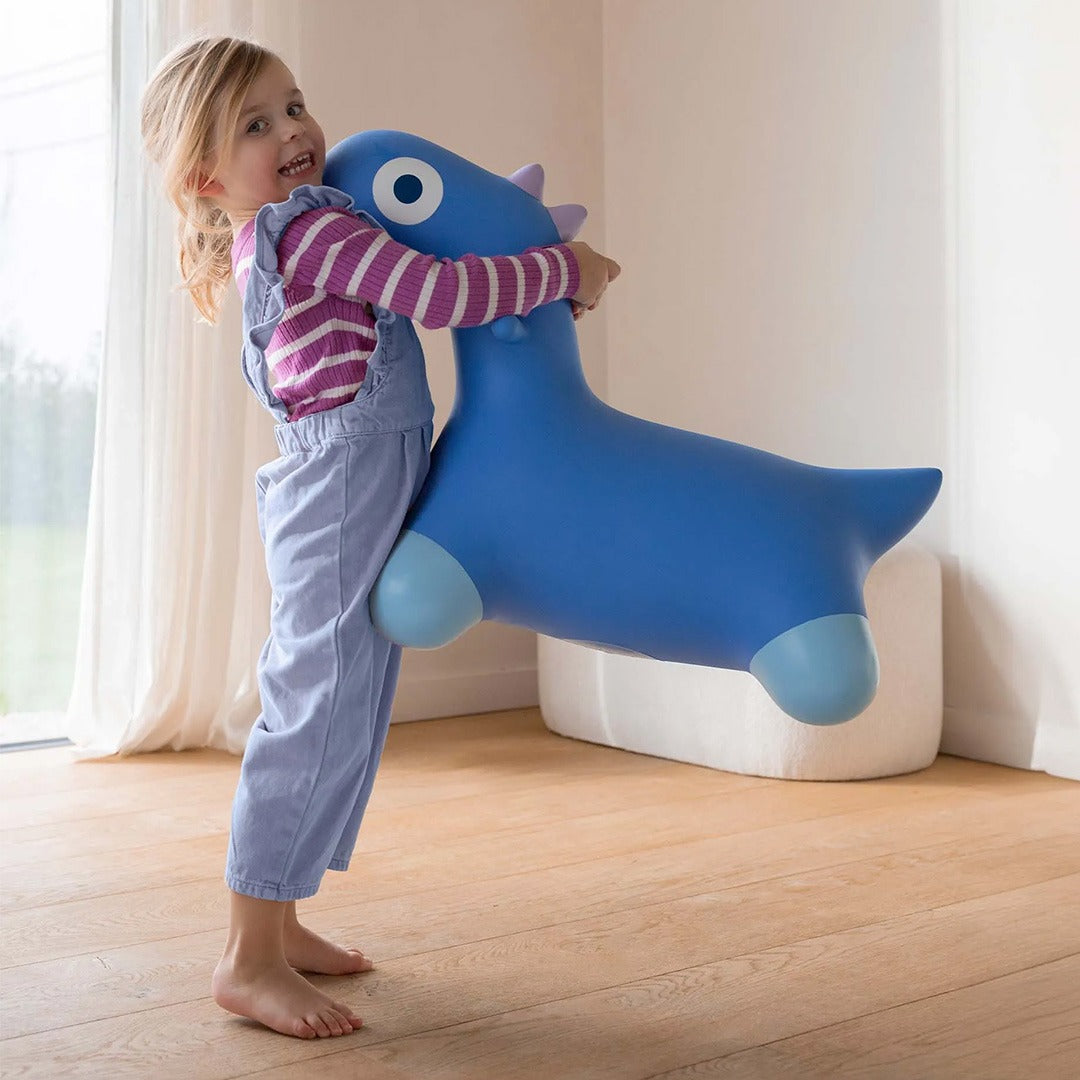 Een meisje knuffelt het blauwe opblaasbare dino skippydier.