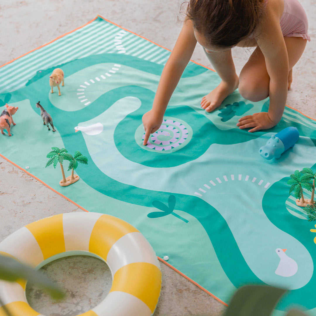 Een kind speelt met speelgoed op de quut groene safari speelhanddoek met dieren en een waterbaan.