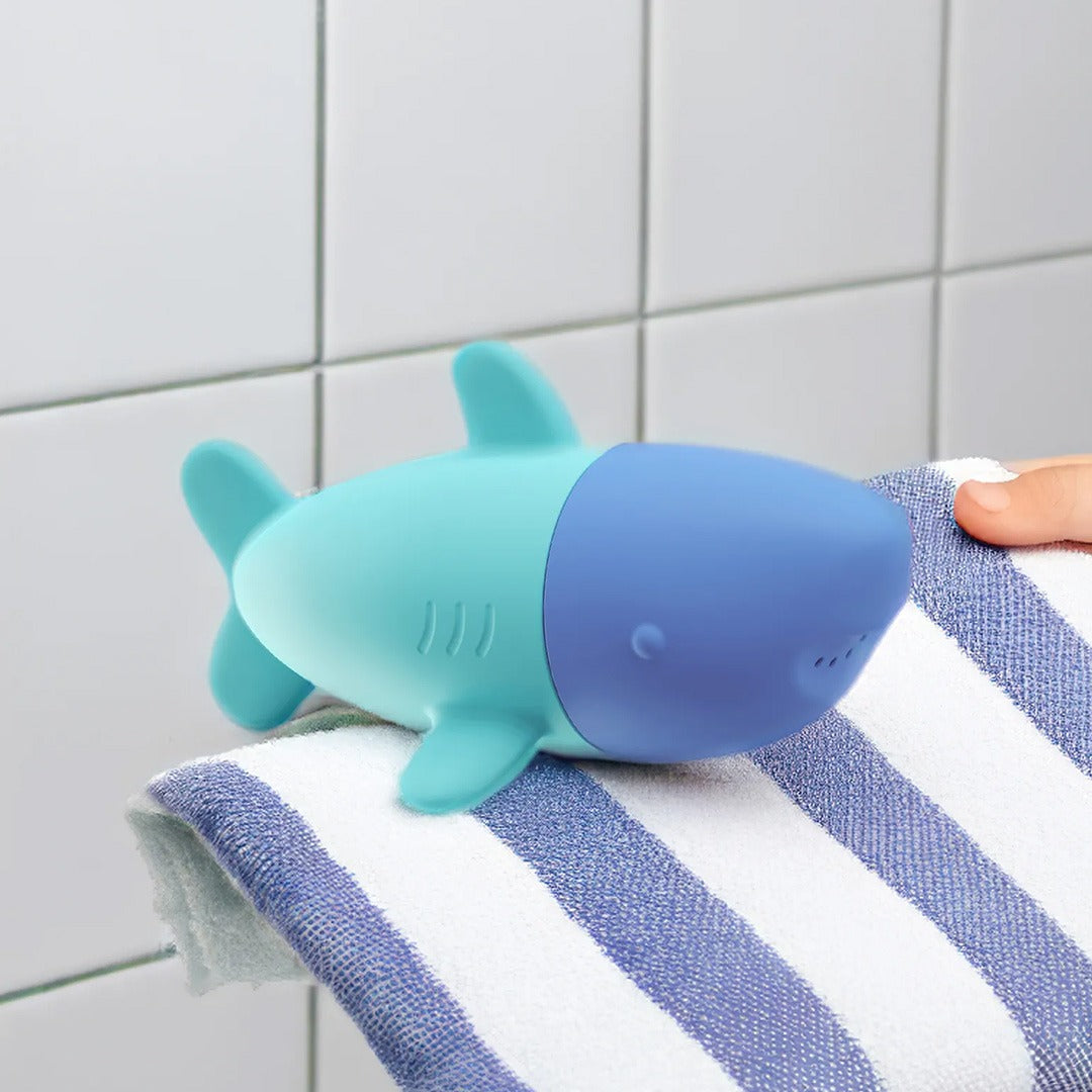 De blauw-turquoise haai badspeelgoed sproeier ligt op een blauw-wit gestreepte handdoek.