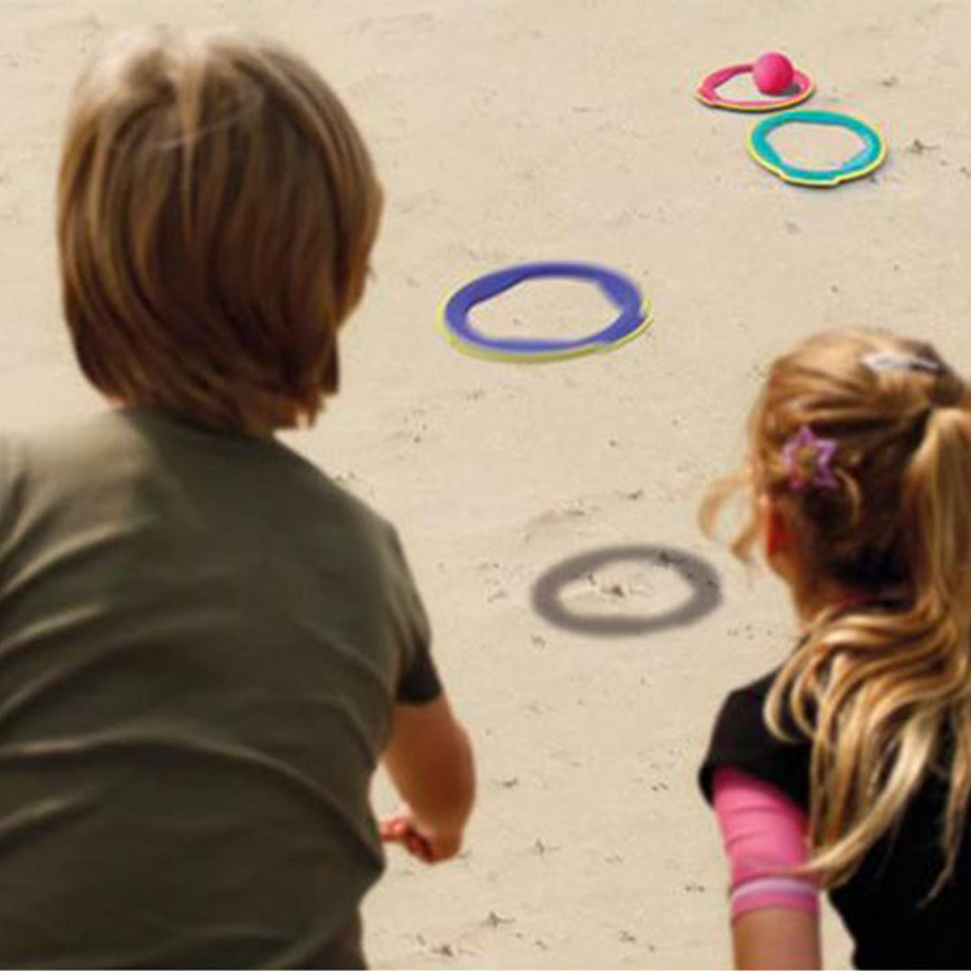 Twee kinderen spelen met de Quut Ringo ringen en bal op een zandstrand.